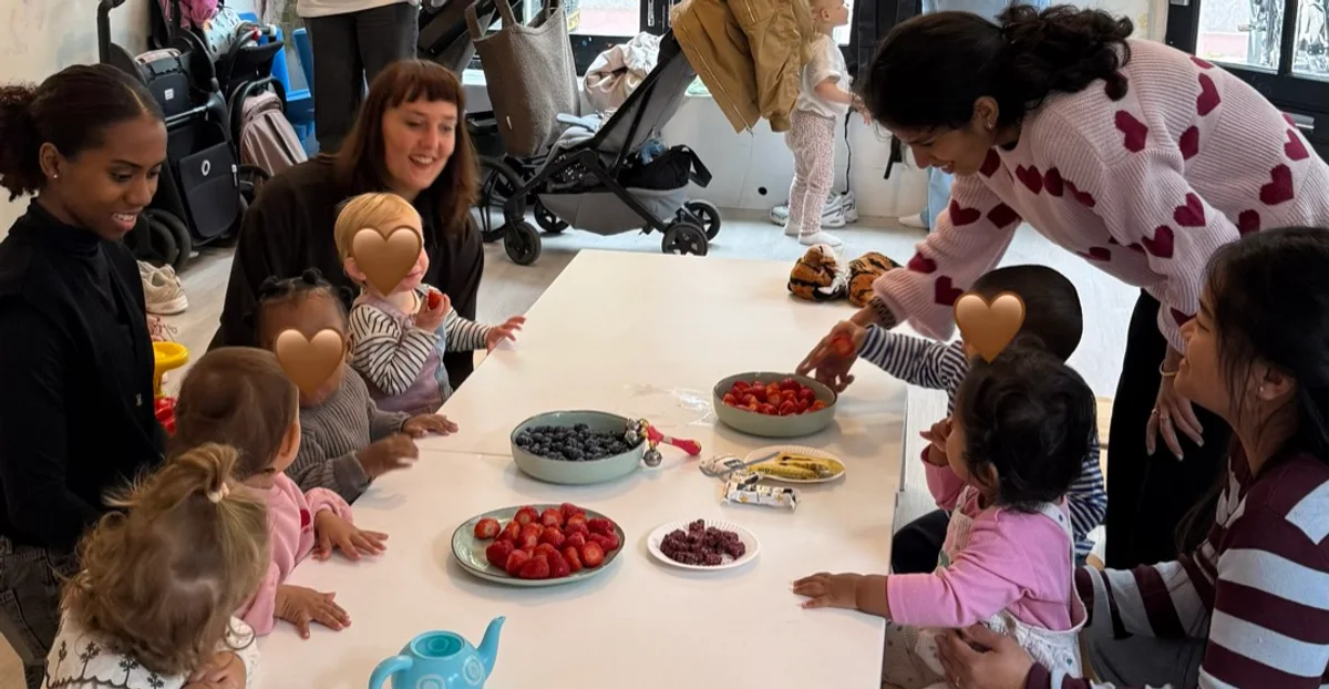 Moms and little ones gathered around a table with fruit and snacks at the first Mama Circle Playdate