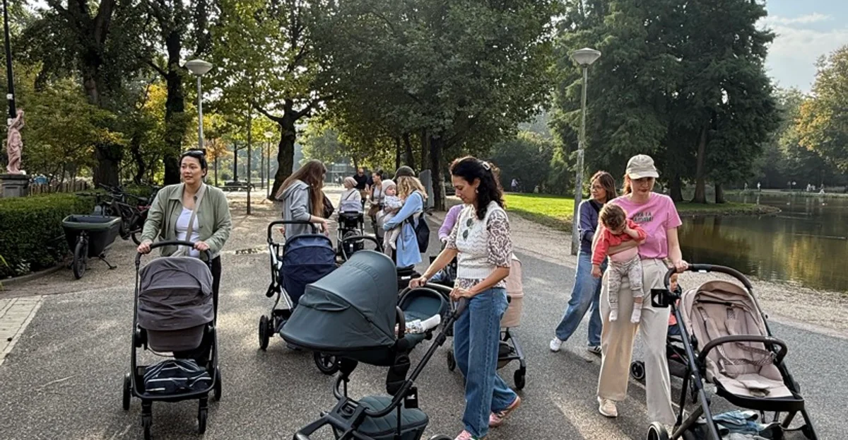 A large group of moms, babies and little ones walking with strollers through Vondelpark